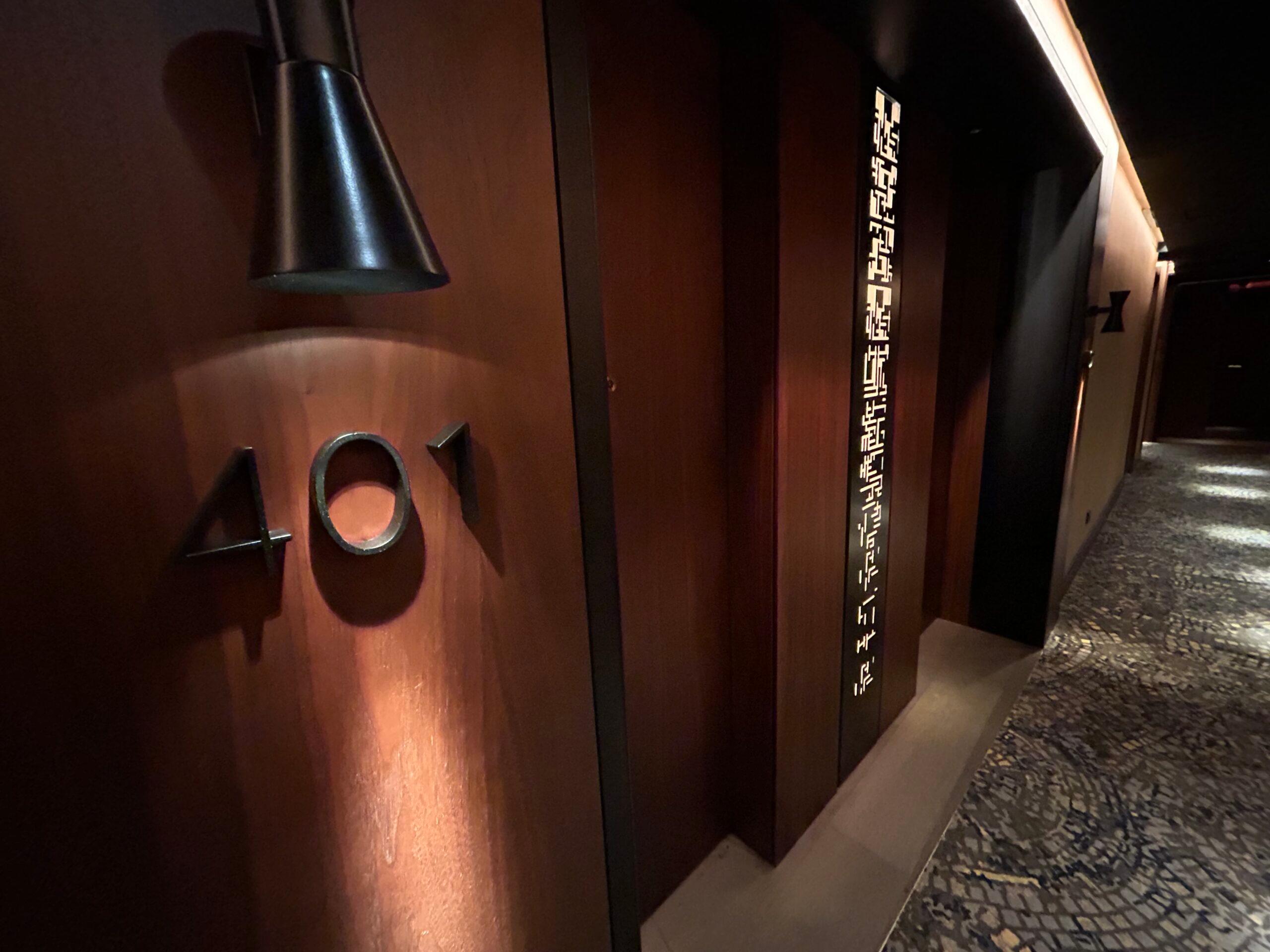 Moody hallway lighting showing a "401" number block to denote a hotel room. 